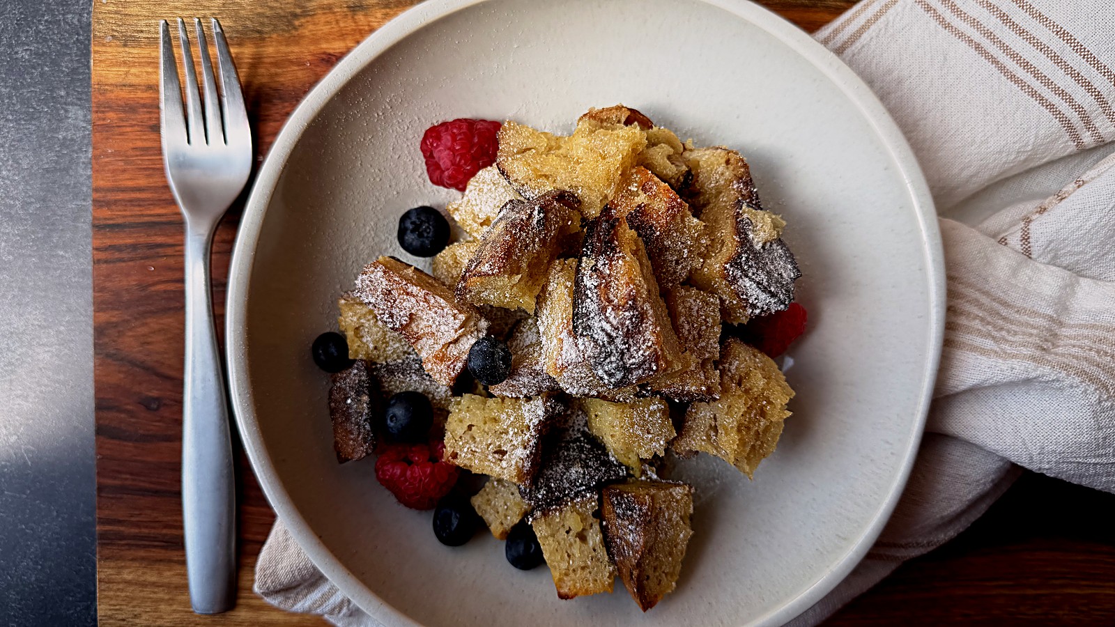 Serving of French toast casserole with blueberries and raspberries on a white plate beside a fork.