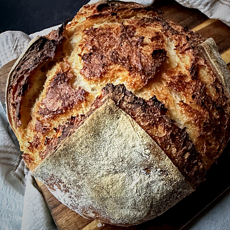 Crusty round loaf of bread with a flour-dusted top on a wooden board.