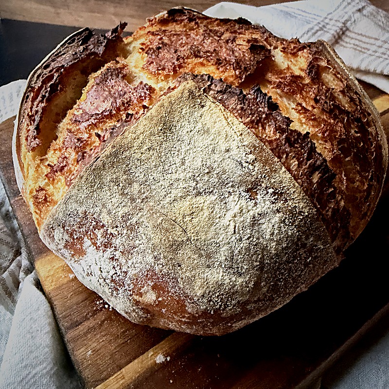Rustic round bread loaf with a crackled golden crust on a towel-lined board.