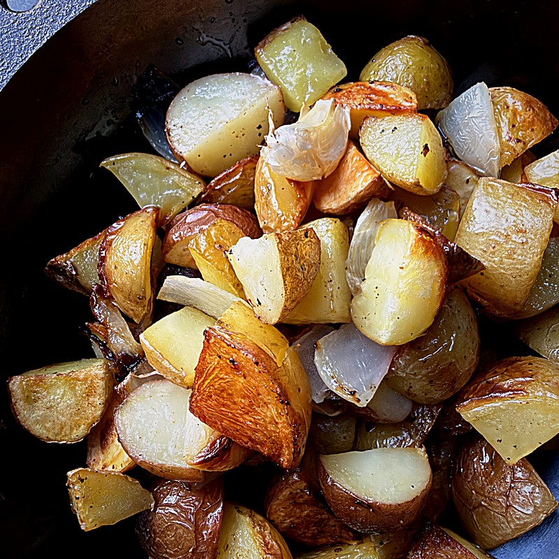 Golden roasted potato chunks with onion in a cast iron skillet.