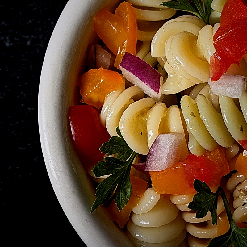 Close-up of rotini pasta salad with tomatoes, orange peppers, and red onion.