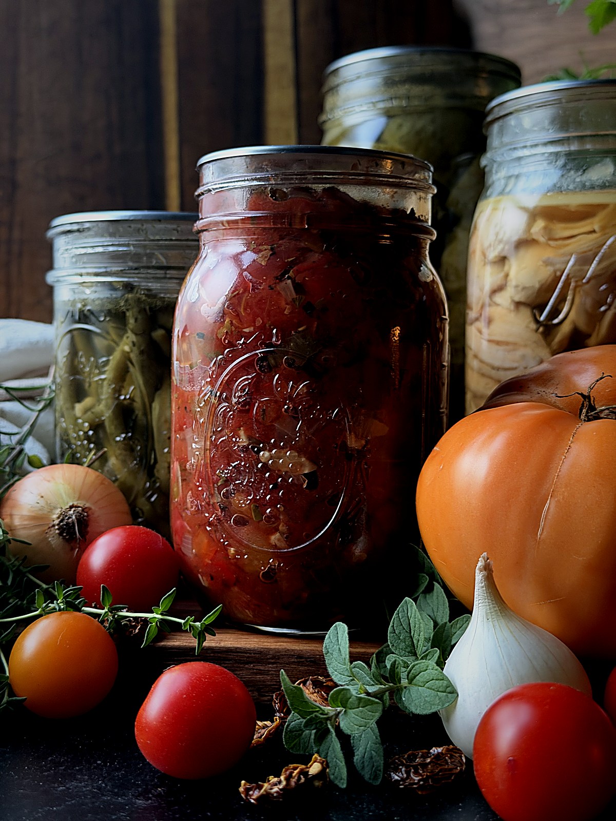 Home-canned tomatoes in a mason jar with jarred vegetables, fresh tomatoes, and garlic.