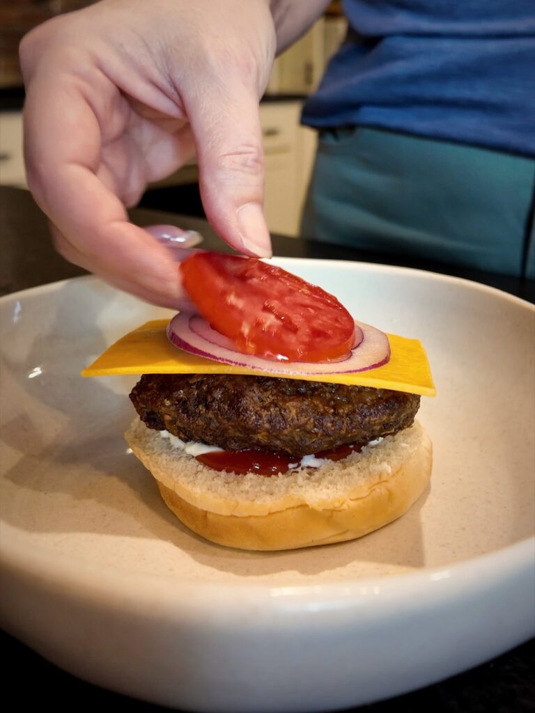 Placing a tomato slice on a cheeseburger with red onion and cheddar