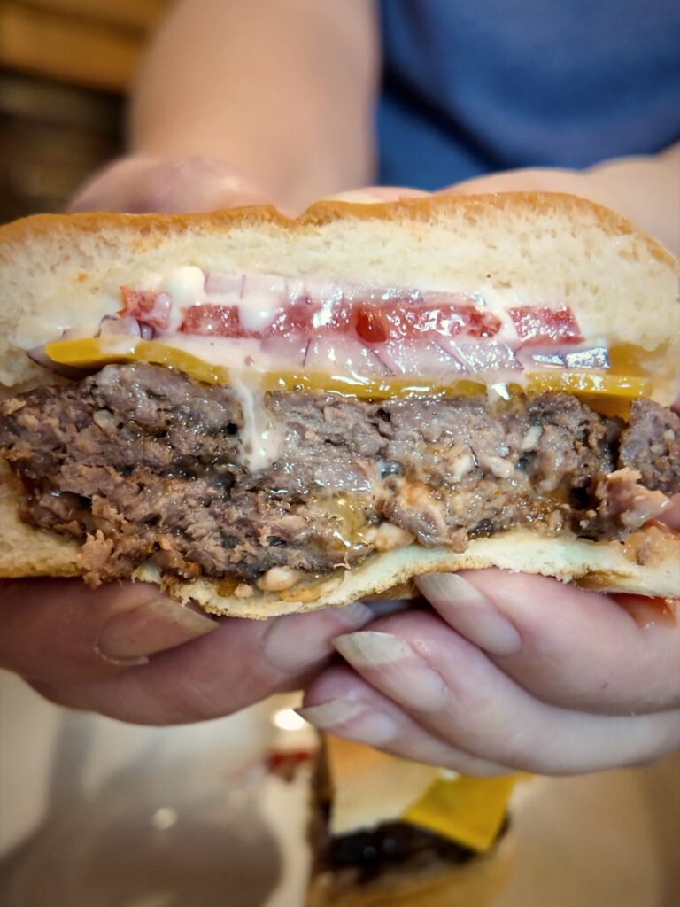 Cheeseburger with tomato and red onion, cut in half and held in two hands