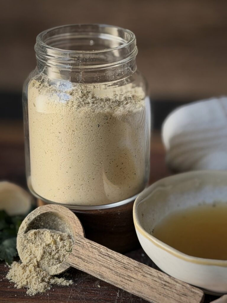 Close-up of a glass jar filled with chicken bouillon powder, with a wooden scoop of powder in front