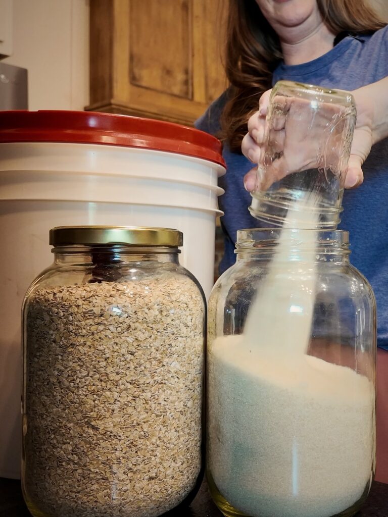 Filling glass jars of oats and a white dry staple in front of a storage bucket