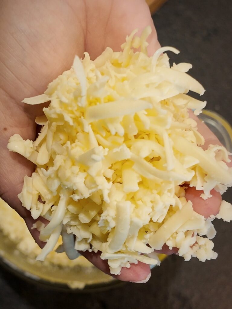 Hand holding a pile of freshly shredded cheese next to a cheese block