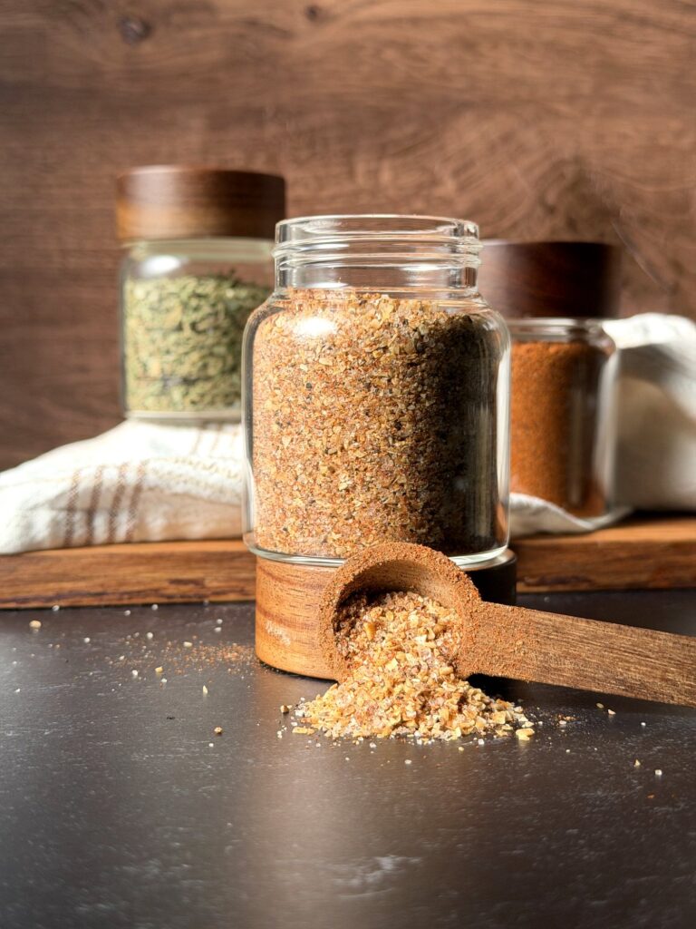 Homemade burger seasoning in a glass spice jar with a wooden scoop