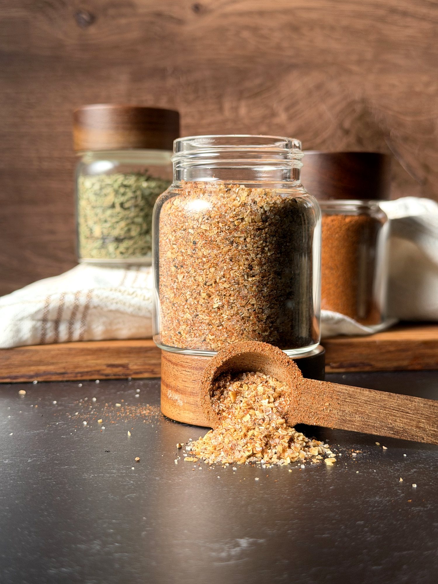 Homemade burger seasoning in a glass spice jar with a wooden scoop