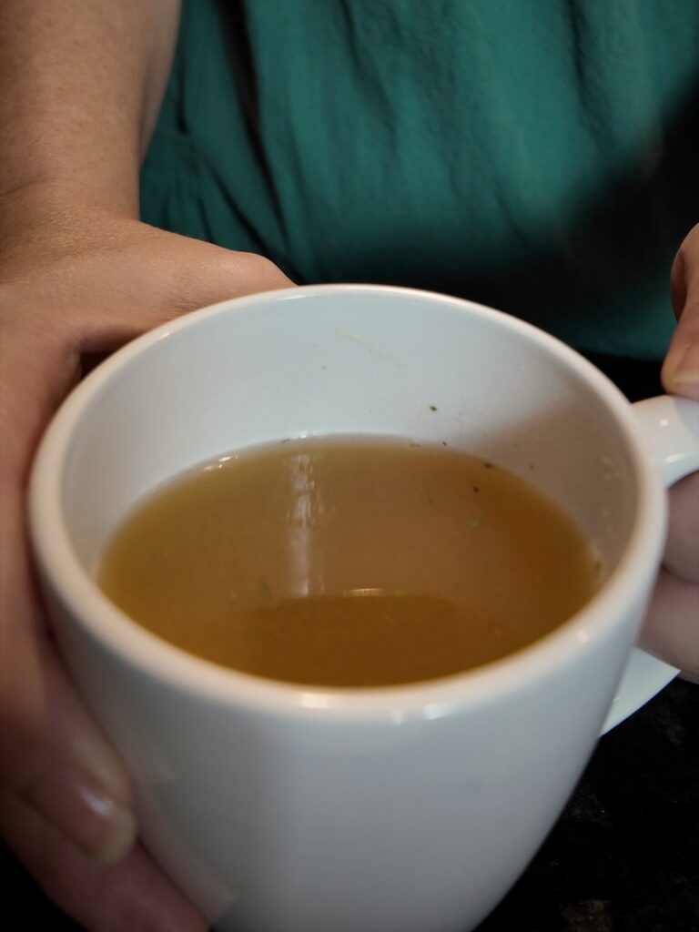 Hands holding a white mug of golden chicken broth