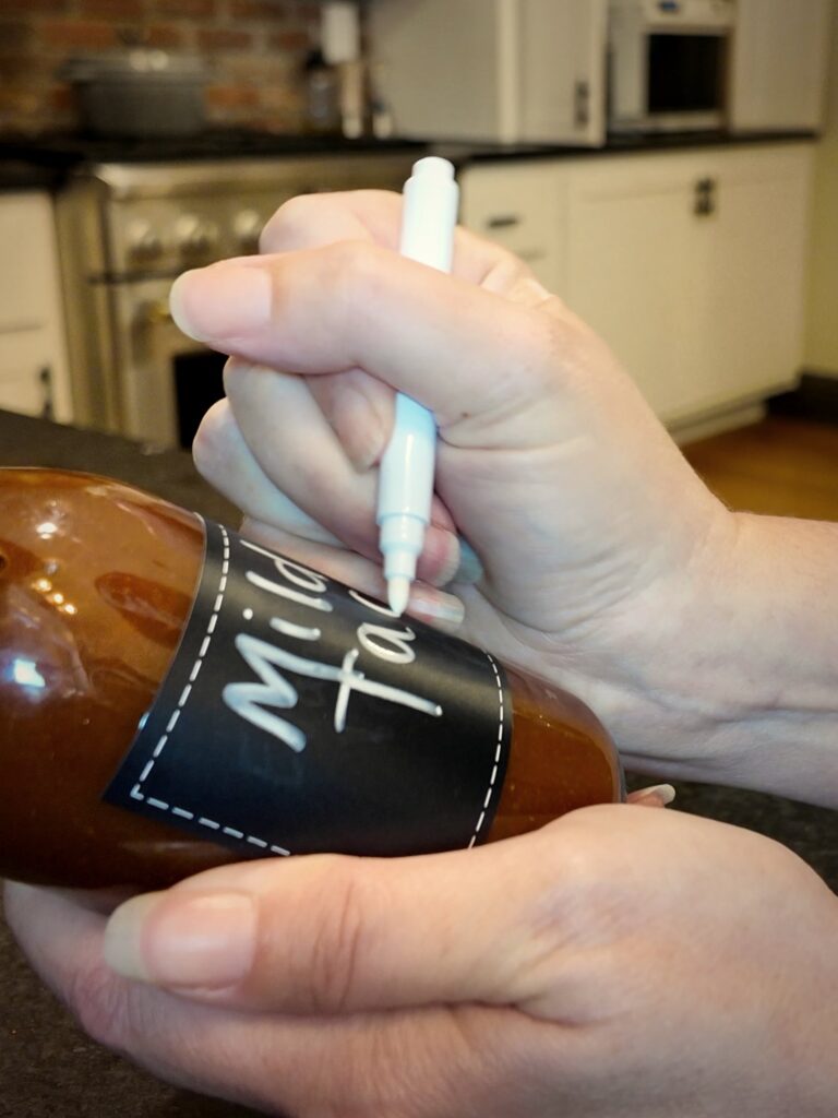 Writing a label on a bottle of homemade mild taco sauce with a white marker