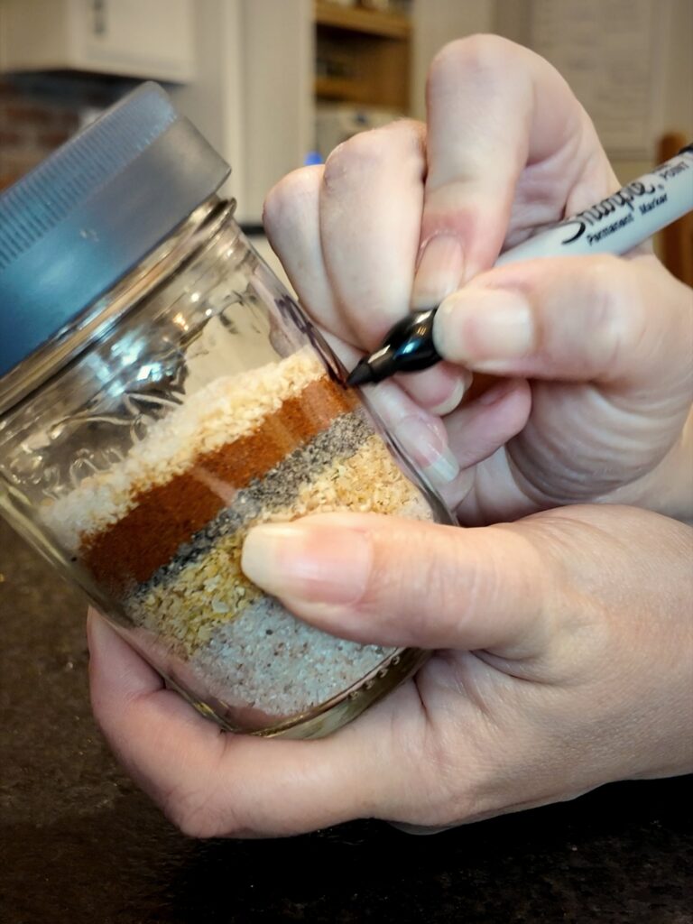 Labeling a jar of layered burger seasoning ingredients with a marker