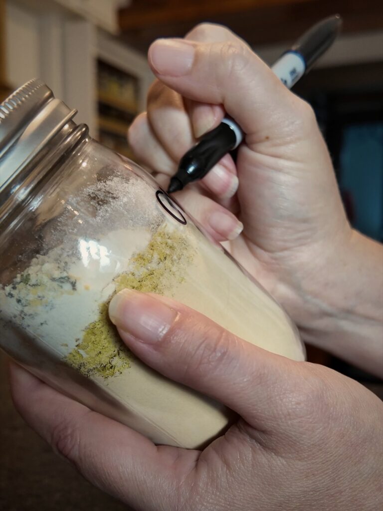 Hand writing on a glass jar of layered chicken bouillon powder with a marker