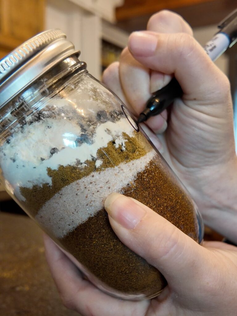 Hand labeling a mason jar of layered chili seasoning spices with a marker
