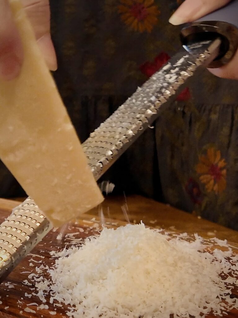 Microplane grater shaving a wedge of Parmesan into a fluffy pile on a wooden board.