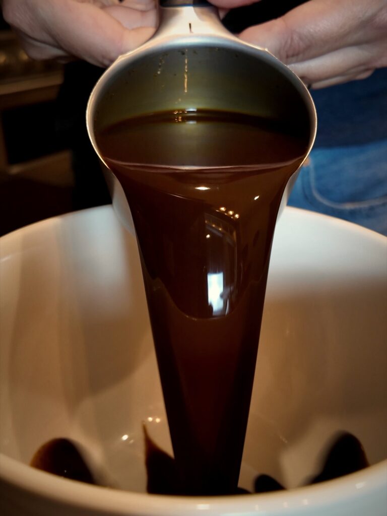 Soy sauce pouring from a metal measuring cup into a white bowl for jerky marinade