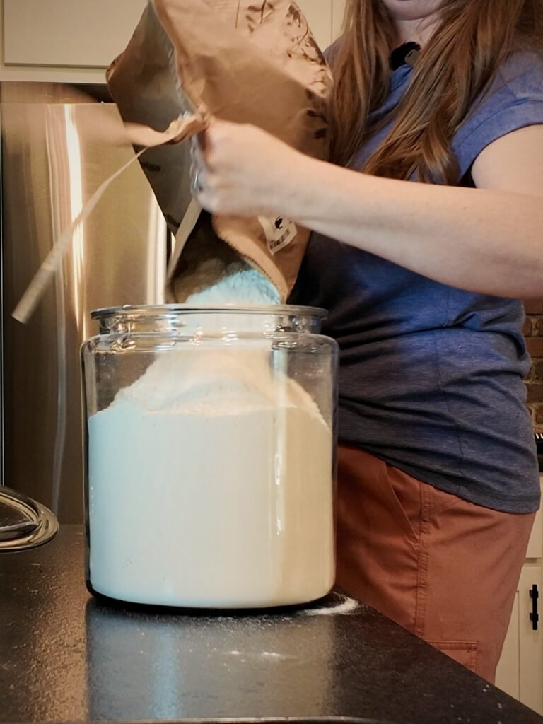 Pouring flour from a large paper bag into a glass storage jar