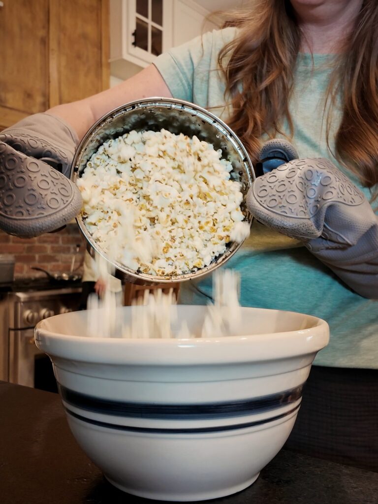 Pouring freshly popped popcorn from a pot into a blue-striped bowl