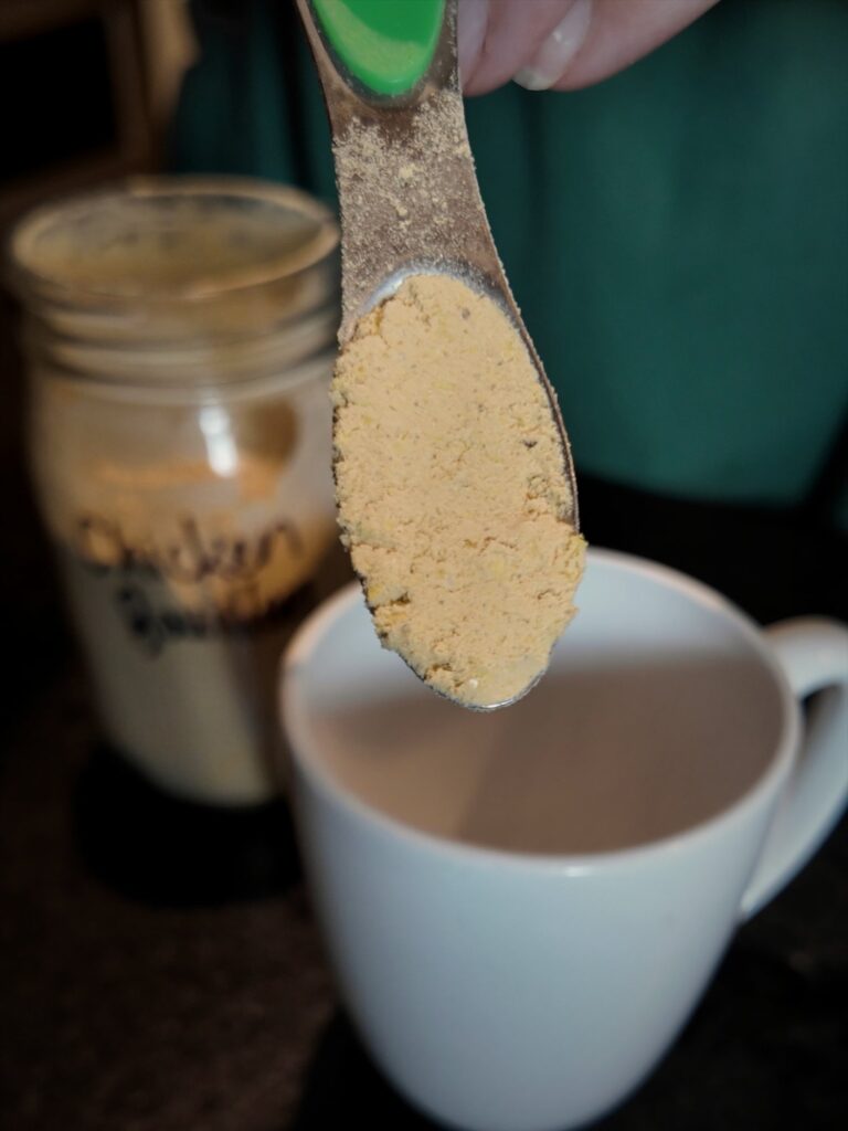 Measuring spoon of chicken bouillon powder over a white mug, with the labeled jar behind it