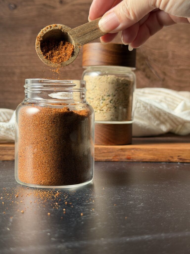 Wooden scoop of chili seasoning being poured into a glass jar