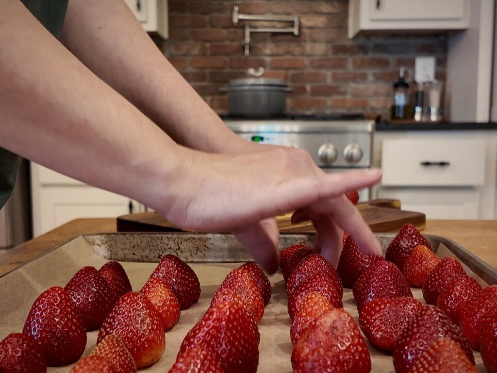 Hands arranging whole strawberries on a parchment-lined sheet pan.
