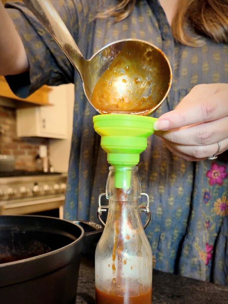 Ladling homemade taco sauce through a green funnel into a swing-top glass bottle