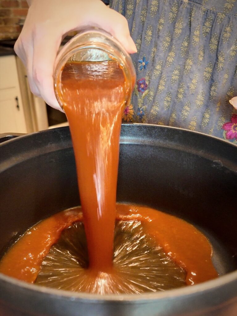 Tomato sauce pouring from a glass jar into a pot