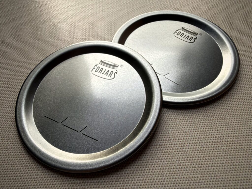 Two ForJars canning lids side by side on a linen surface