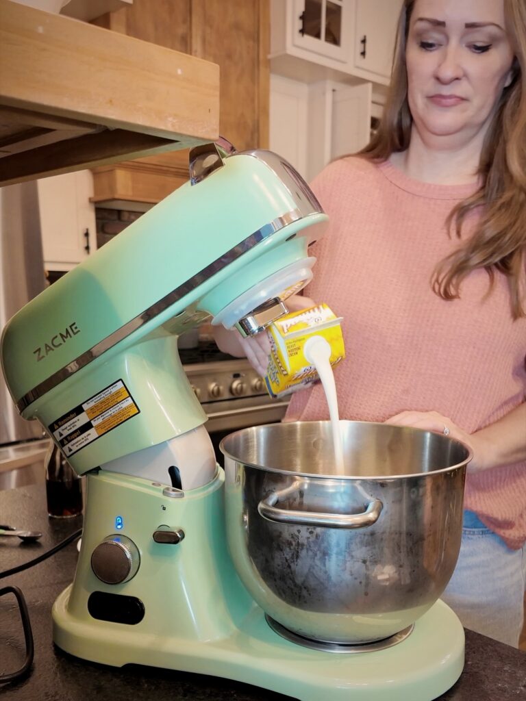 Heavy cream being poured into the bowl of a mint-green stand mixer