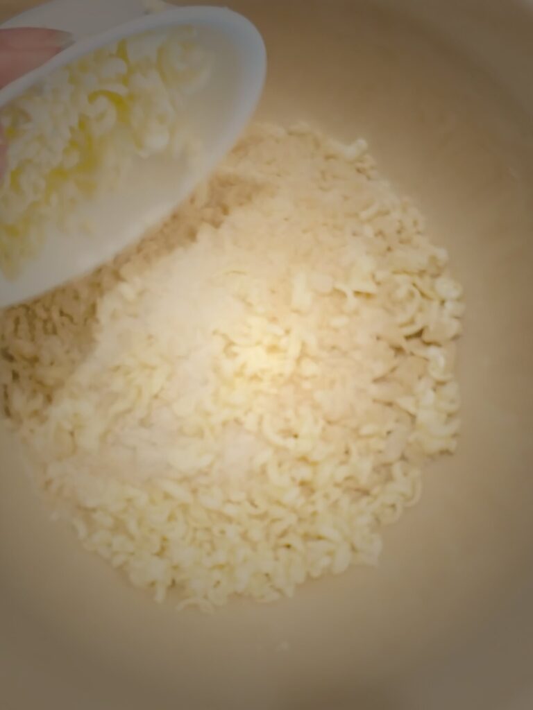 Grated butter being poured from a small white bowl into a crumbly flour mixture in a large bowl