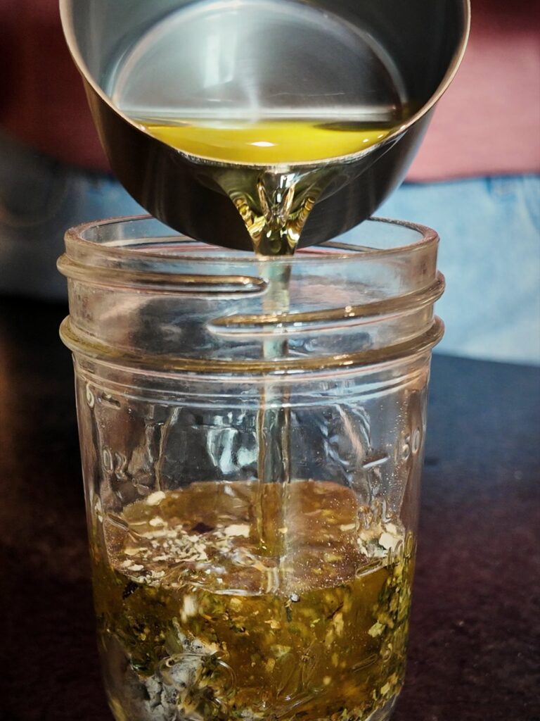 Pouring oil into a small mason jar of Italian dressing mix