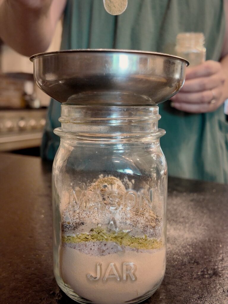 Spooning seasoning through a metal funnel into a mason jar layered with powders