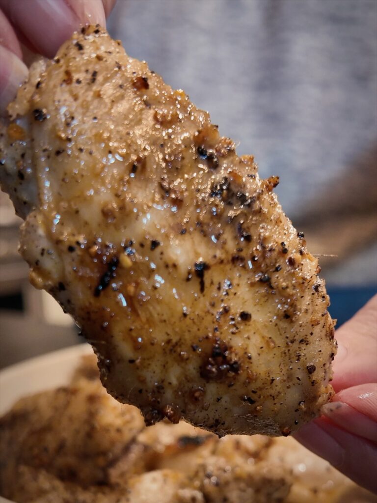 Hand holding a chicken wing coated in lemon pepper seasoning over a bowl of wings