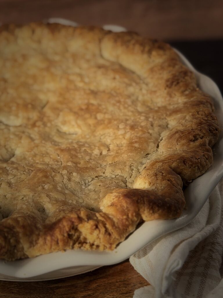 Close-up of the browned, crimped edge of a flaky all-butter pie crust in a white fluted pie dish