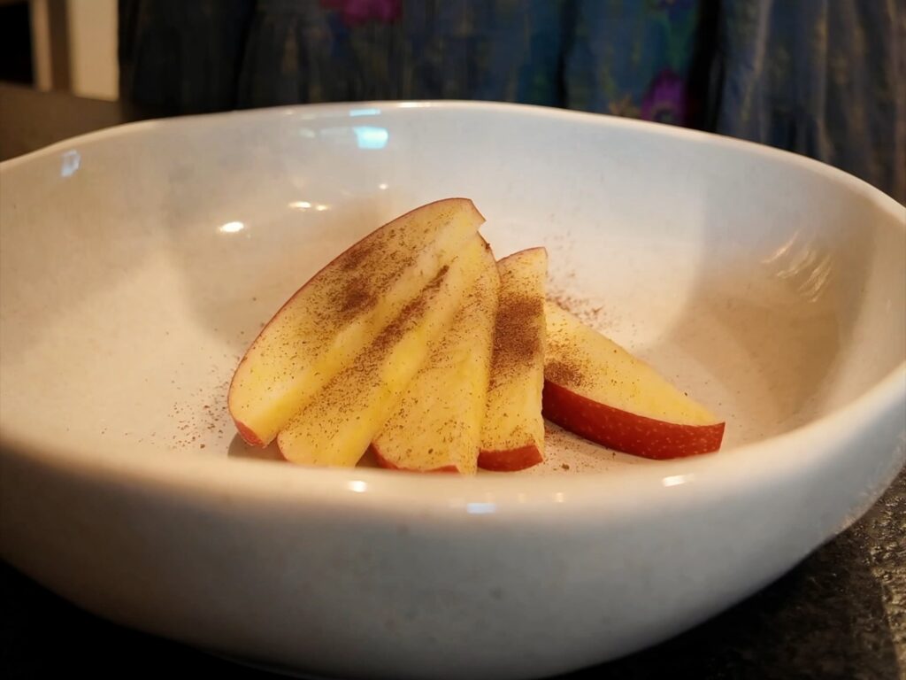 Red apple slices dusted with apple pie spice in a white bowl