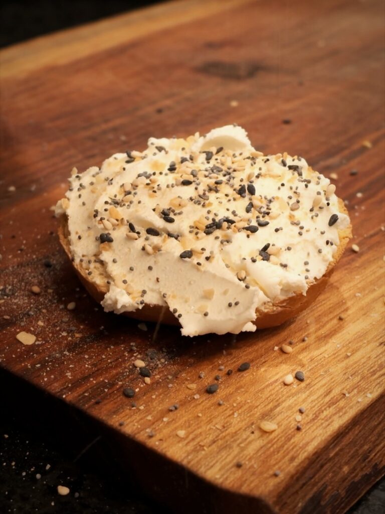 Bagel with cream cheese and everything bagel seasoning on a wooden cutting board