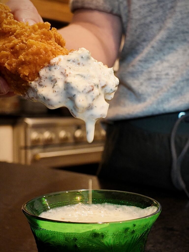 Thick ranch dip clinging to a breaded chicken tender over a green glass bowl