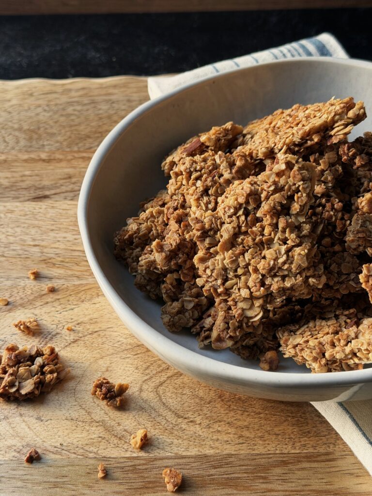 Close-up of thick, chunky granola clusters with visible oats and nut pieces in a white bowl.