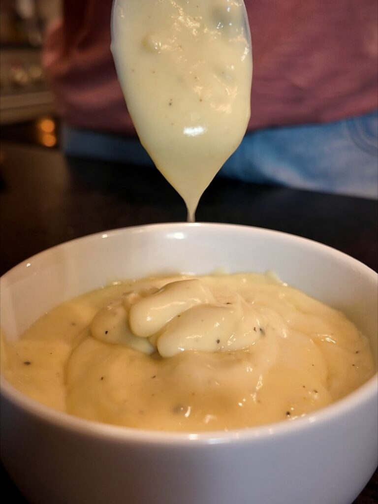 Thick homemade cream soup dripping from a spoon into a white bowl