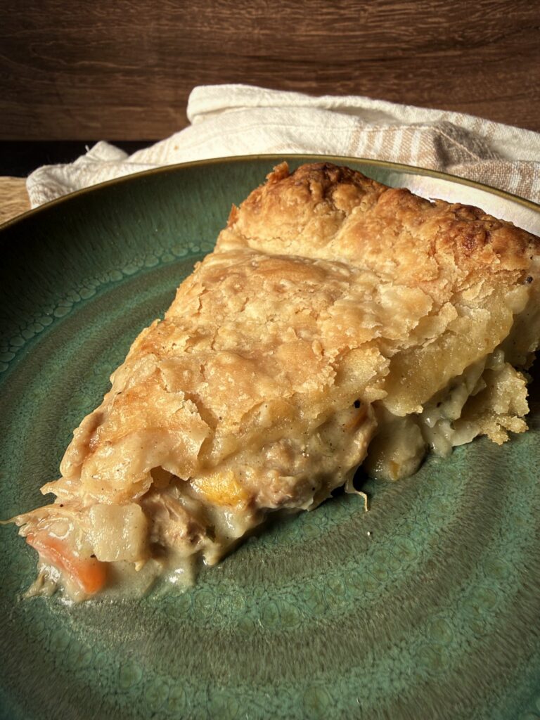 Close-up of a slice of chicken pot pie on a green plate, with creamy filling, chicken, carrots and potatoes under a golden flaky crust