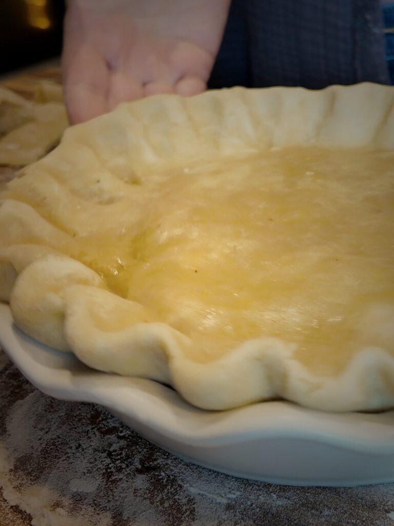 Unbaked double-crust pie with hand-crimped edges in a white fluted pie dish on a floured board