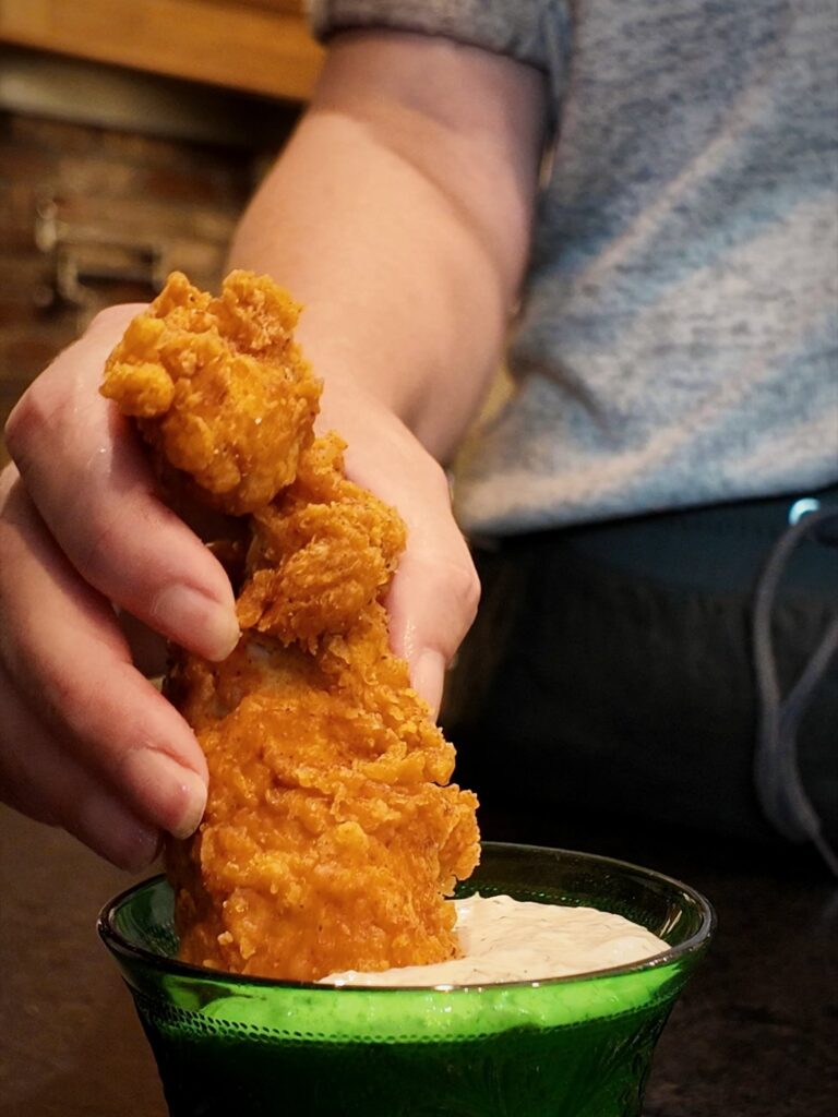 Dipping a breaded chicken tender into a green glass bowl of homemade ranch