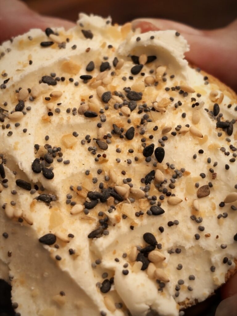 Close-up of everything bagel seasoning sprinkled over cream cheese on a bagel