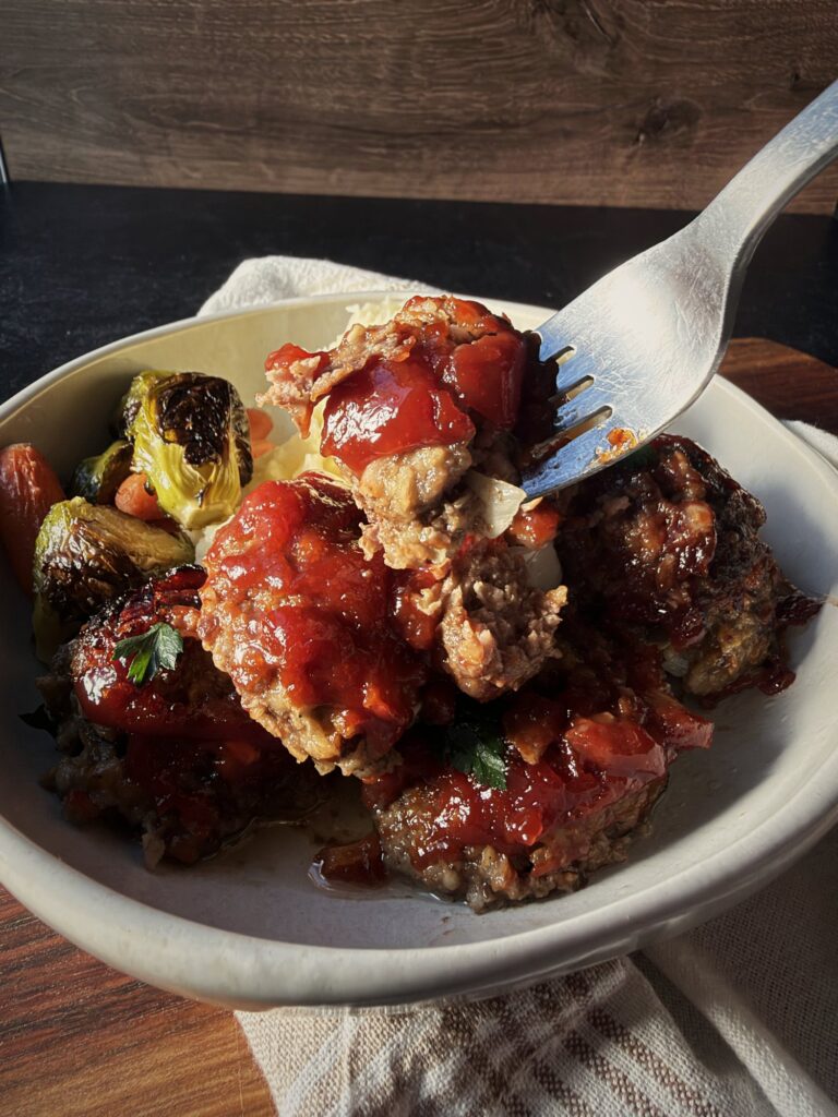 Fork breaking open a sauced meatball in a bowl, showing the tender inside.