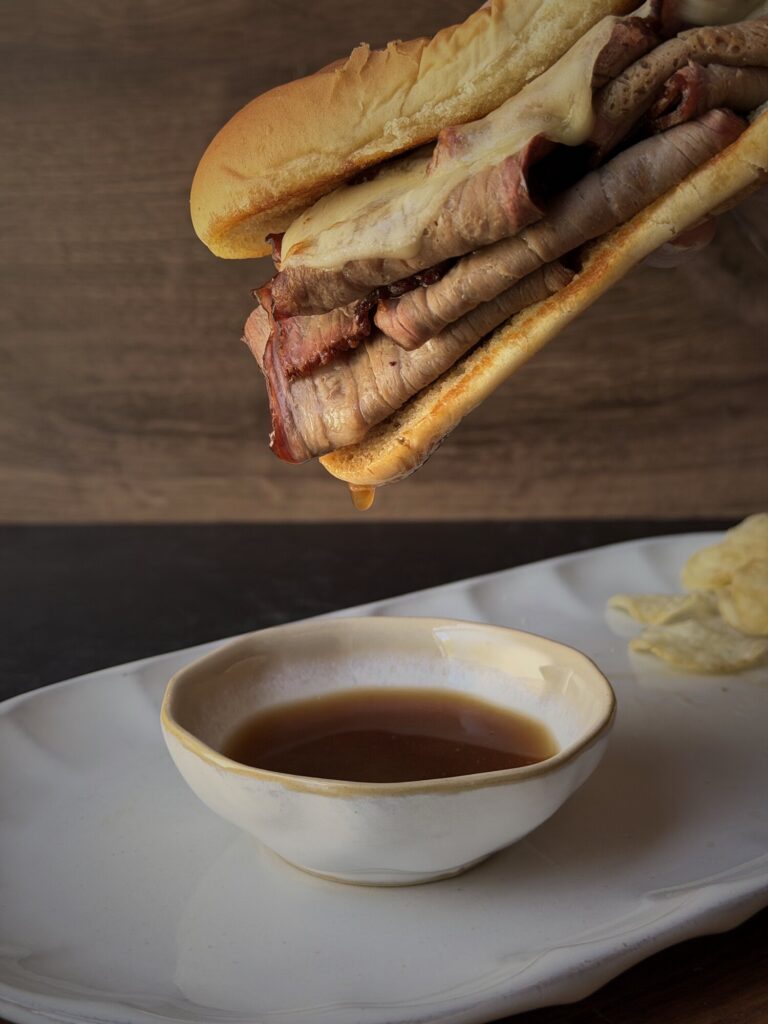 French dip sandwich lifted above a small bowl of homemade au jus