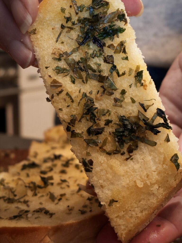 Hand holding a slice of garlic bread topped with homemade Italian seasoning