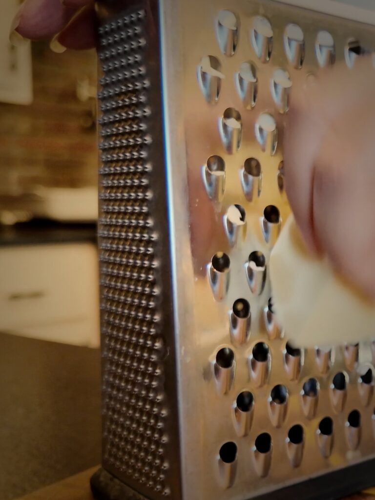 Hand grating a block of frozen butter on the large holes of a stainless steel box grater