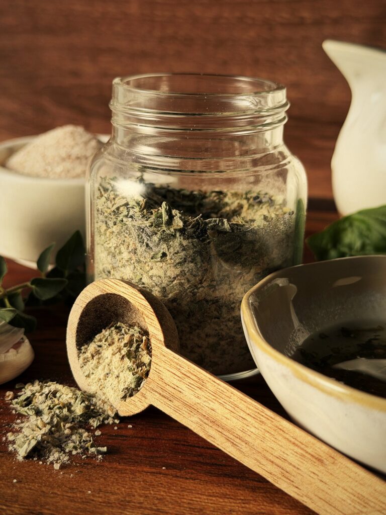 Glass jar of homemade Italian dressing mix with a wooden scoop of the dried herb blend spilling onto a wooden board