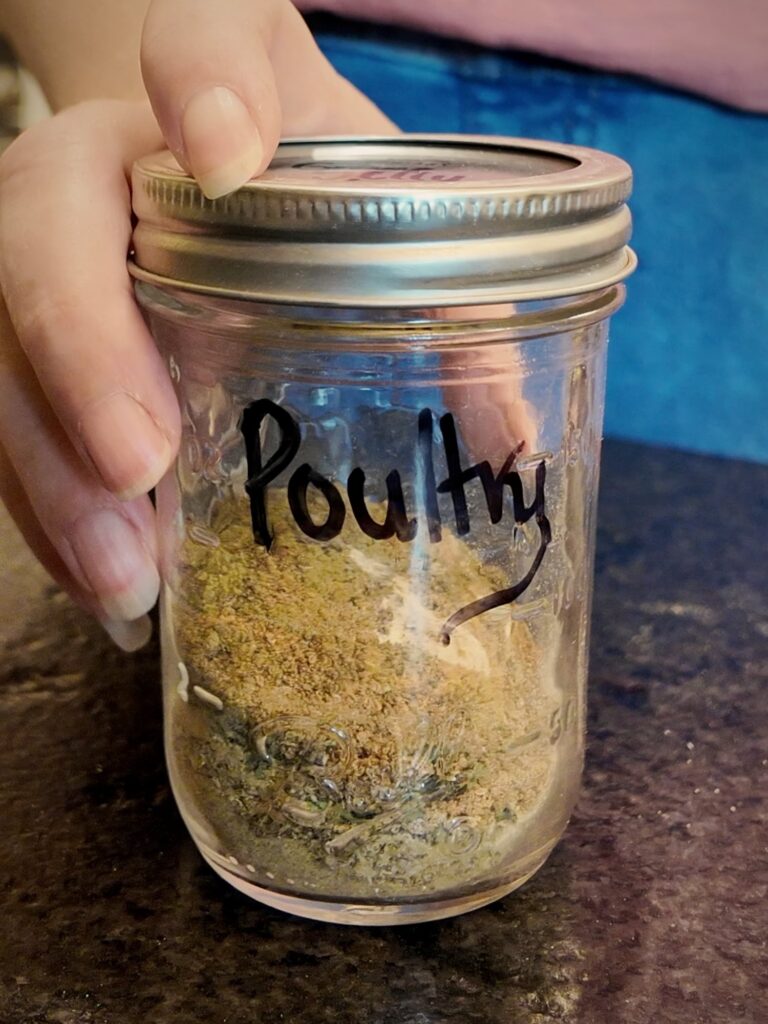 Hand holding a glass jar of homemade poultry seasoning labeled Poultry
