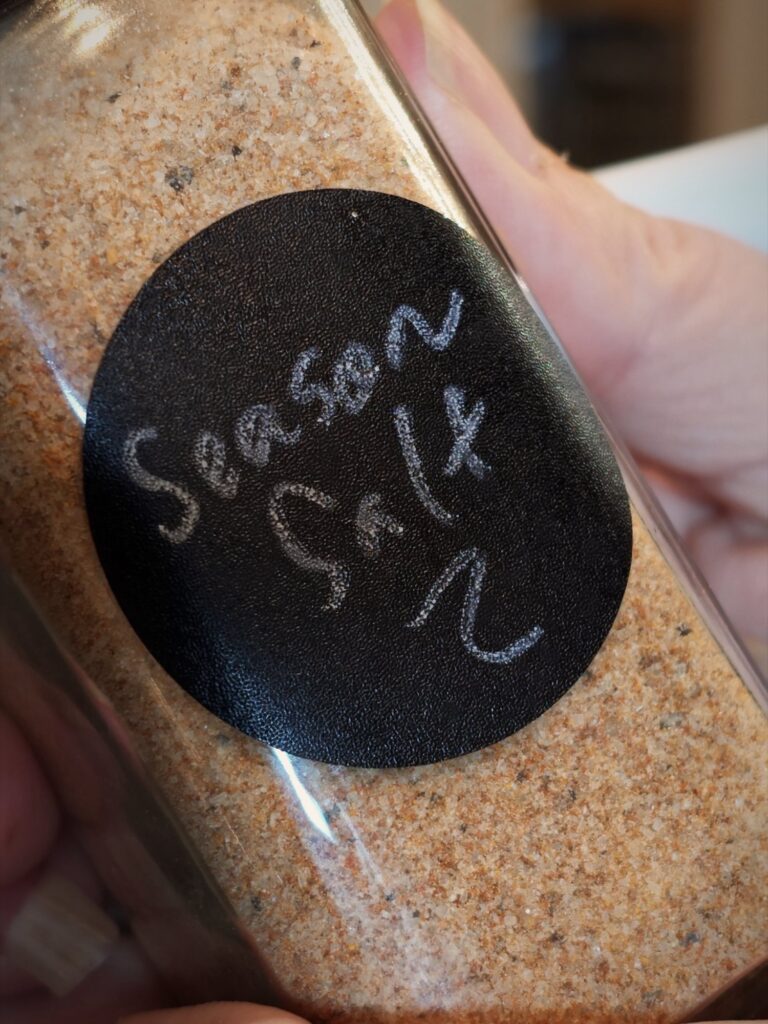 Glass spice jar of seasoned salt with a black label reading Season Salt